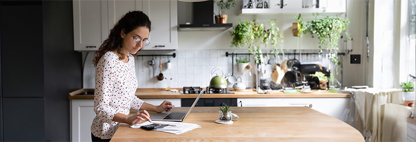 mobile banner of woman indoors at home using laptop computer on kitchen table, Nov 2023 blog, Travis CU,