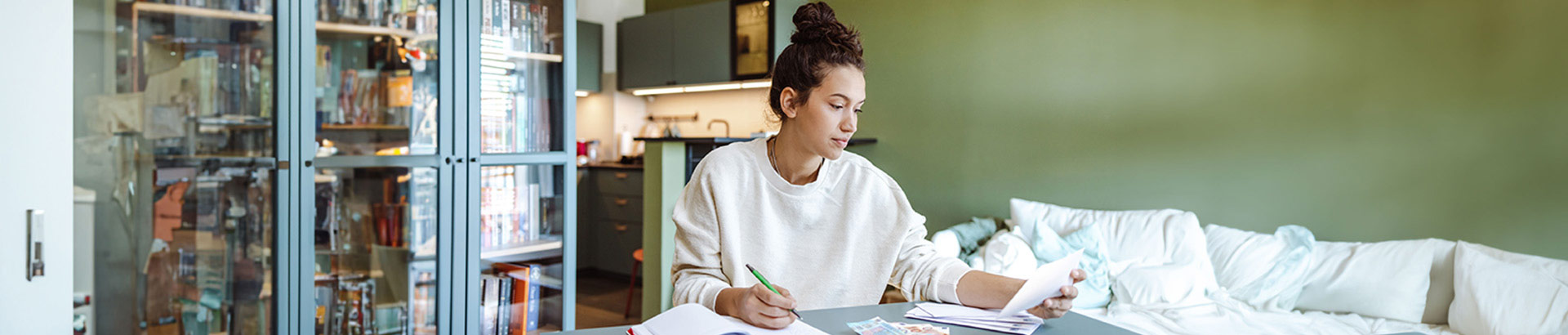 photo of a woman sitting at a table in living room of a home paying bills, Aug 2023 blog, Travis CU,