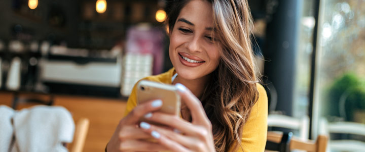 smiling happy woman with straight brunette hair wearing a yellow shirt sitting in a restaurant