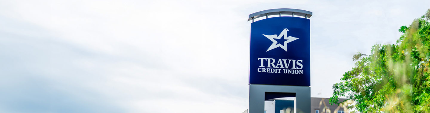 About Us, large photo of the Travis CU headquarters monument signage, outdoors, cloudy day overcast with a green tree on right side,