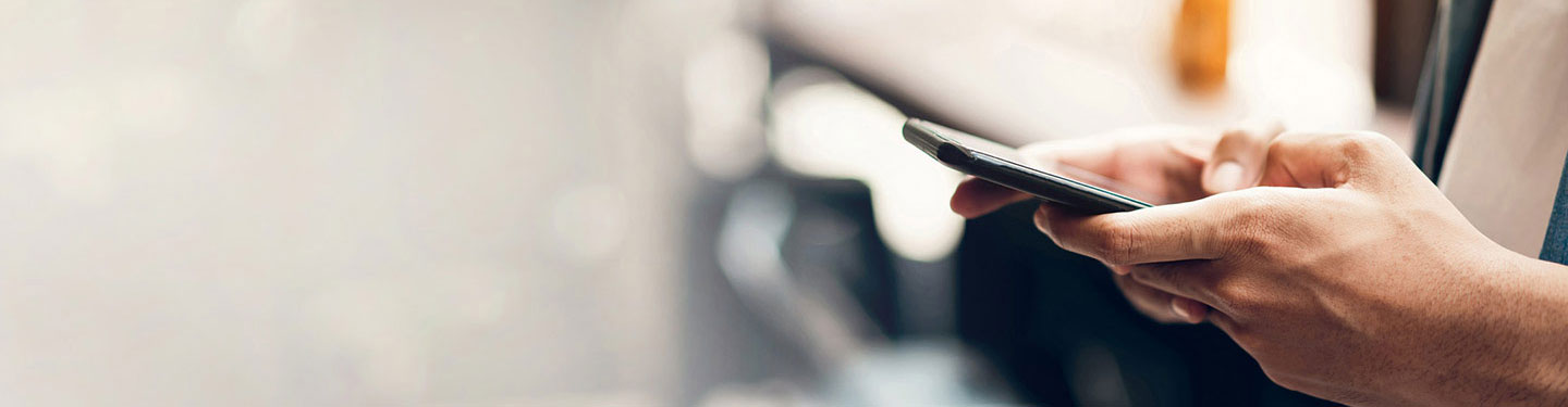 desktop banner close up view of hands holding a smart phone, side view, blurred bokeh background